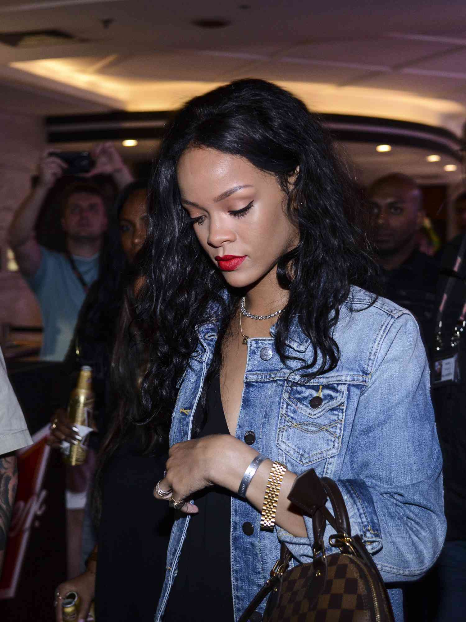 Rihanna wearing a denim jacket, little black dress, Louis Vuitton handbag, and mixed metals jewelry