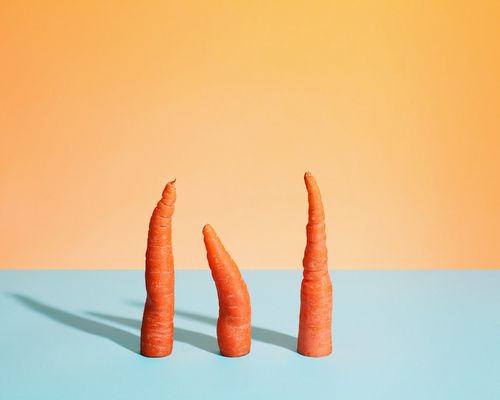 Three cut carrots standing on a flat surface