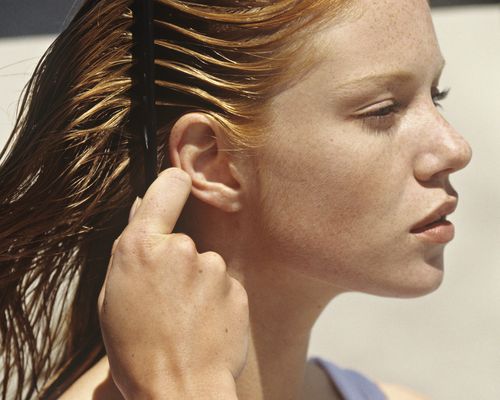 Red haired woman combing her hair in the sunlight.