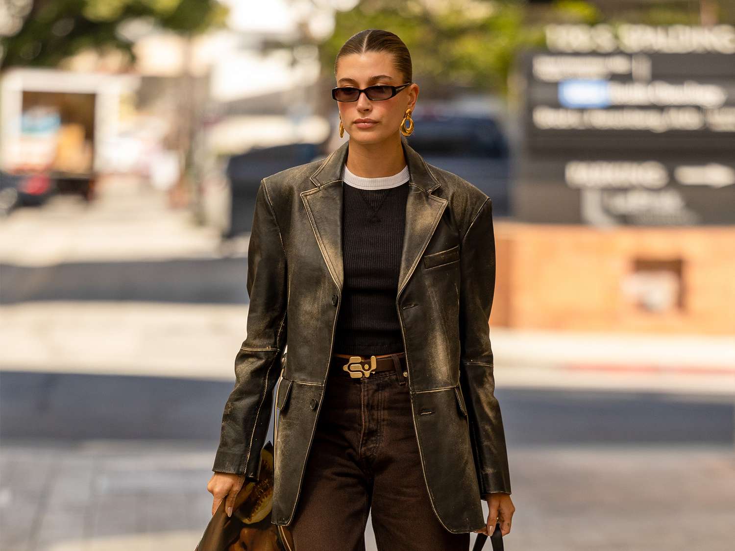 Hailey Bieber wears a leather blazer with a black top with white collar and brown denim pants