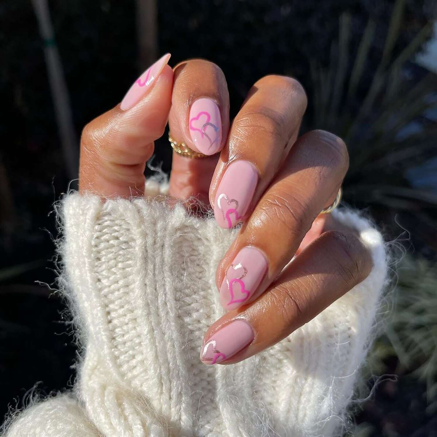 A baby pink manicure with hot pink and silver chrome heart designs