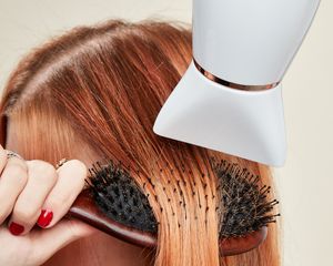 Close up of a woman brushing her red hair as she blow dries it