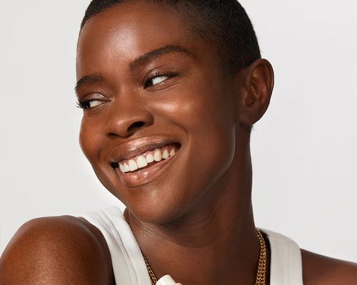 Smiling person looking to the side while holding a makeup bottle against their chest