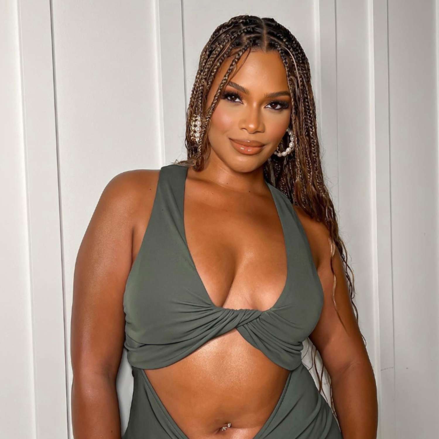 Kamie Crawford posing against white background wearing green cut out dress and pearl earrings