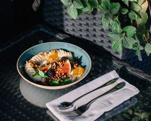 blue bowl of fruit with napkin and silverware on glass table