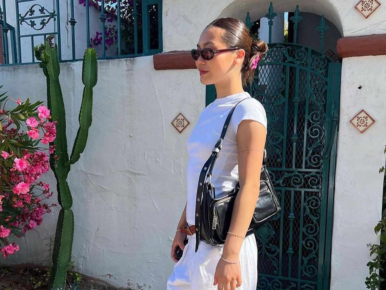 Woman carrying black Marge Sherwood handbag and wearing white outfit, black oval sunglasses, and slicked back bun