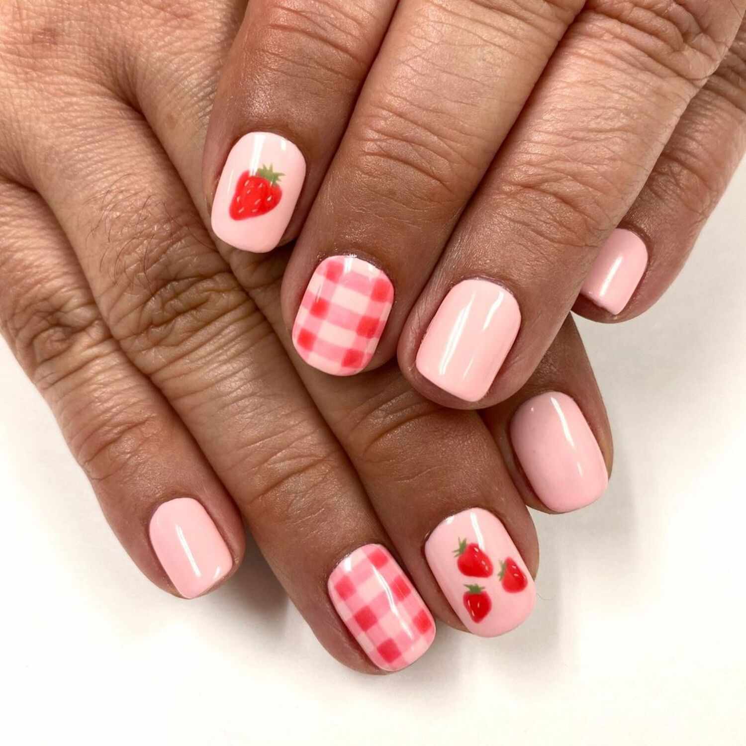 A baby pink manicure with red gingham and strawberry details