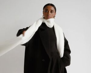 Model wearing black coat, white scarf, and gold hoop earrings