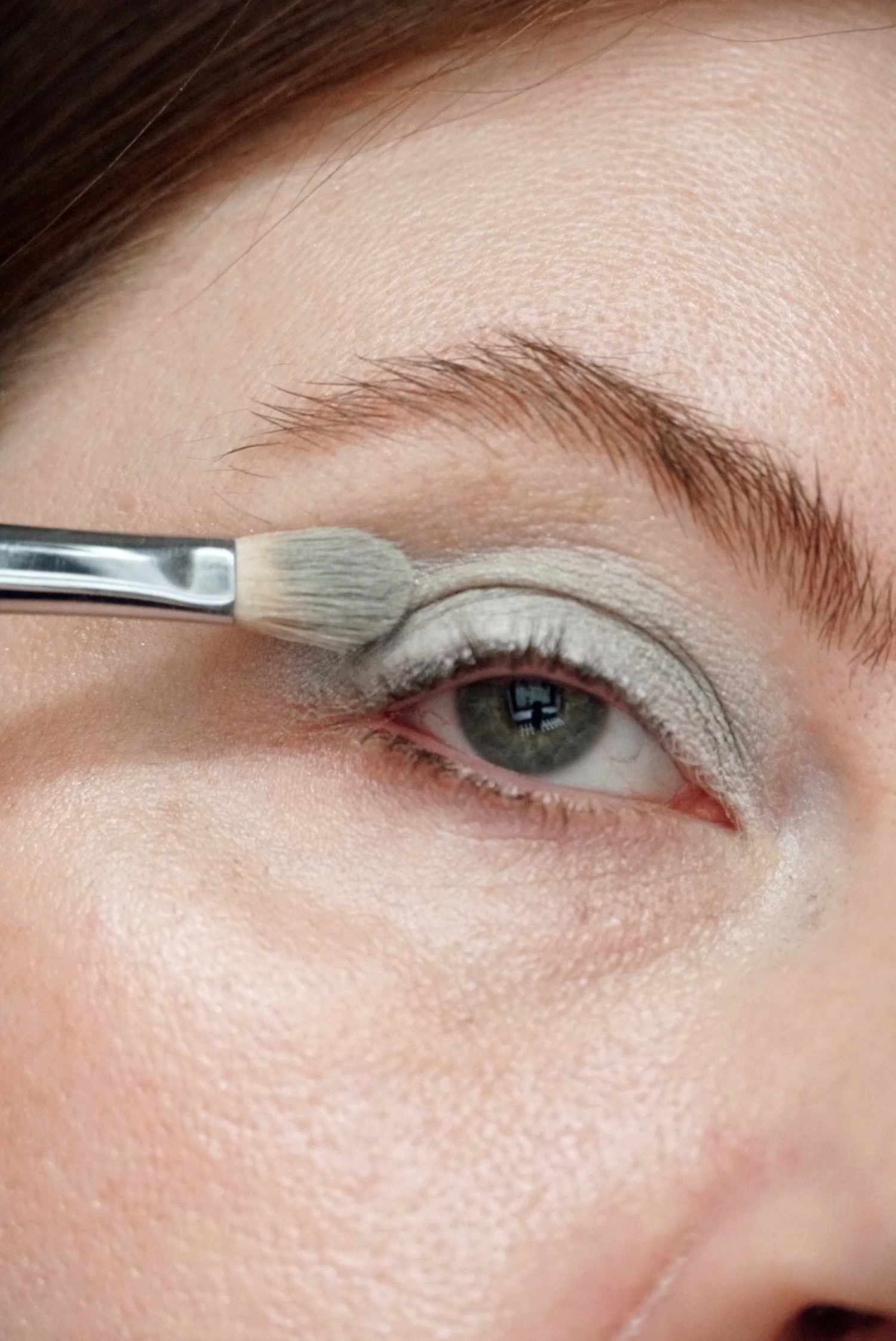 model is applying a light mint green eyeshadow to the eye with a shadow brush