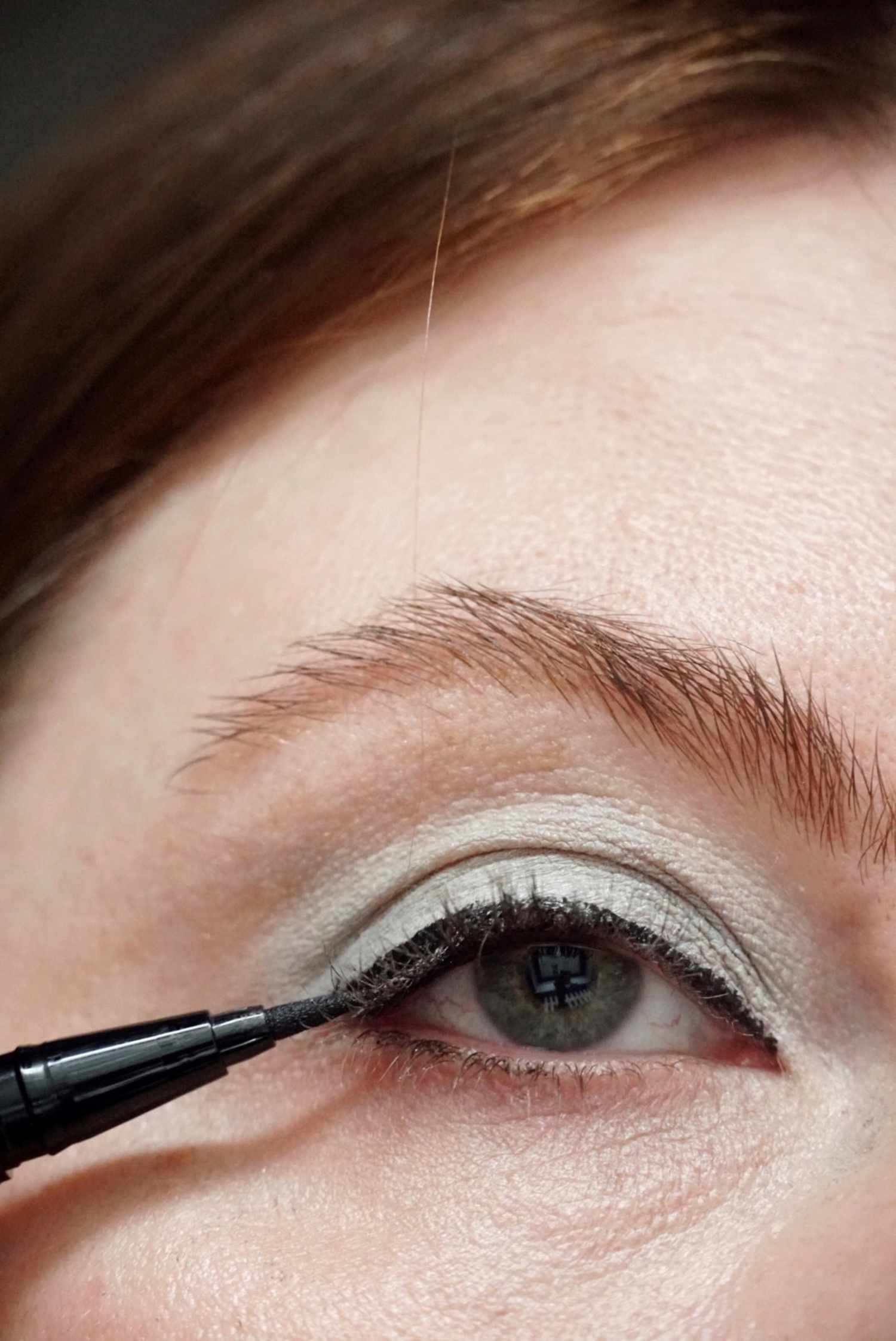 model is applying black liquid eyeliner to the eye 