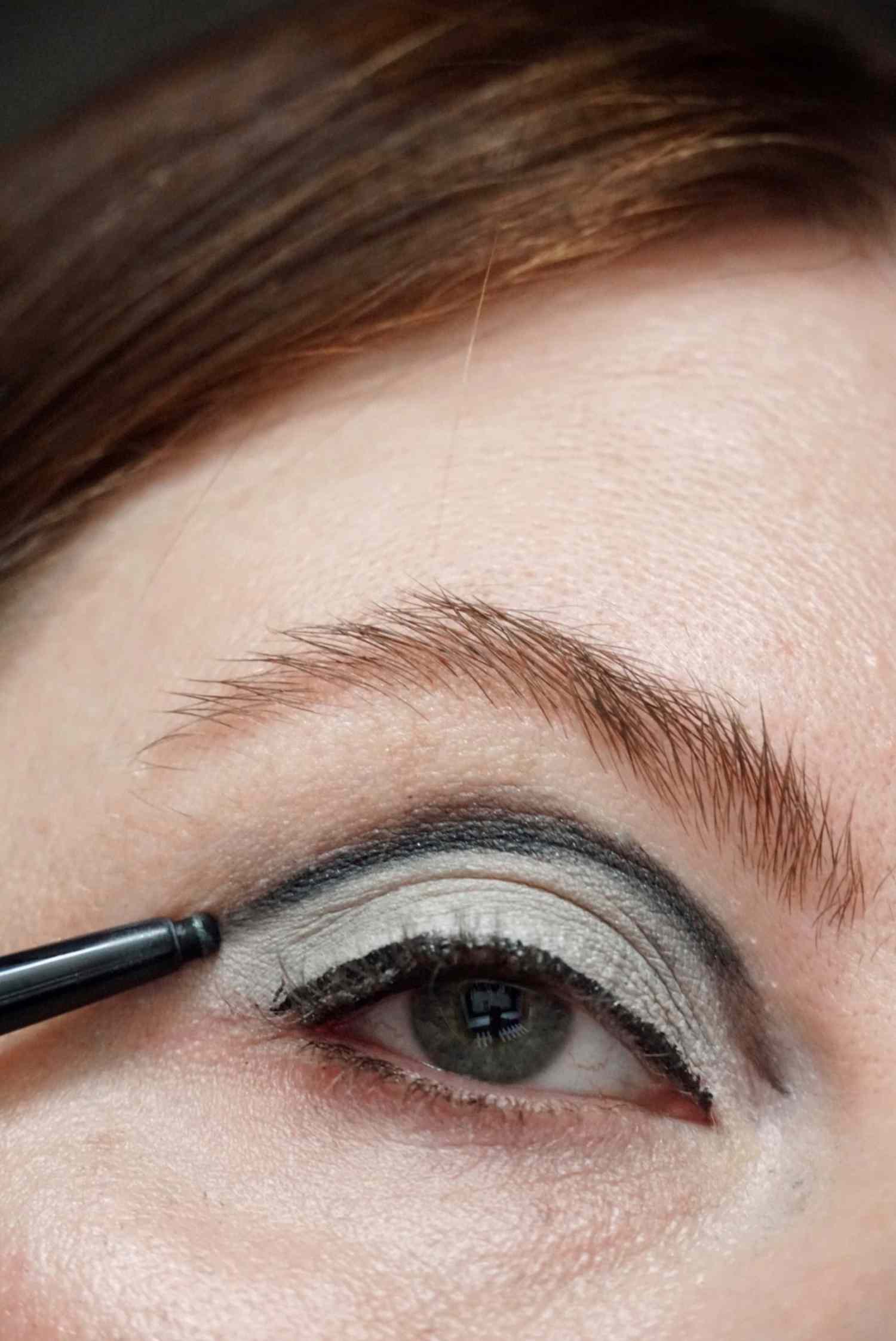 model is applying black eyeliner to the center of the lid 