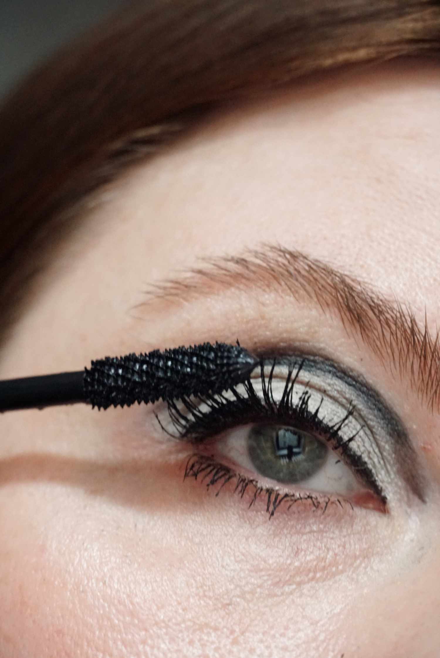 model is applying black mascara to the top eyelashes