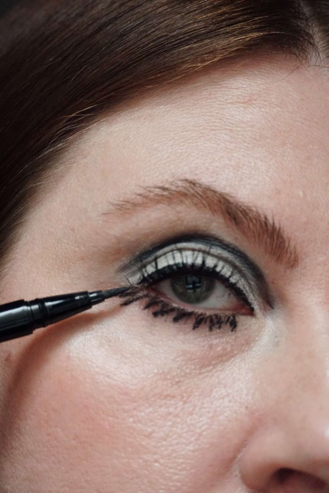 model is applying black liquid liner to the bottom lashes