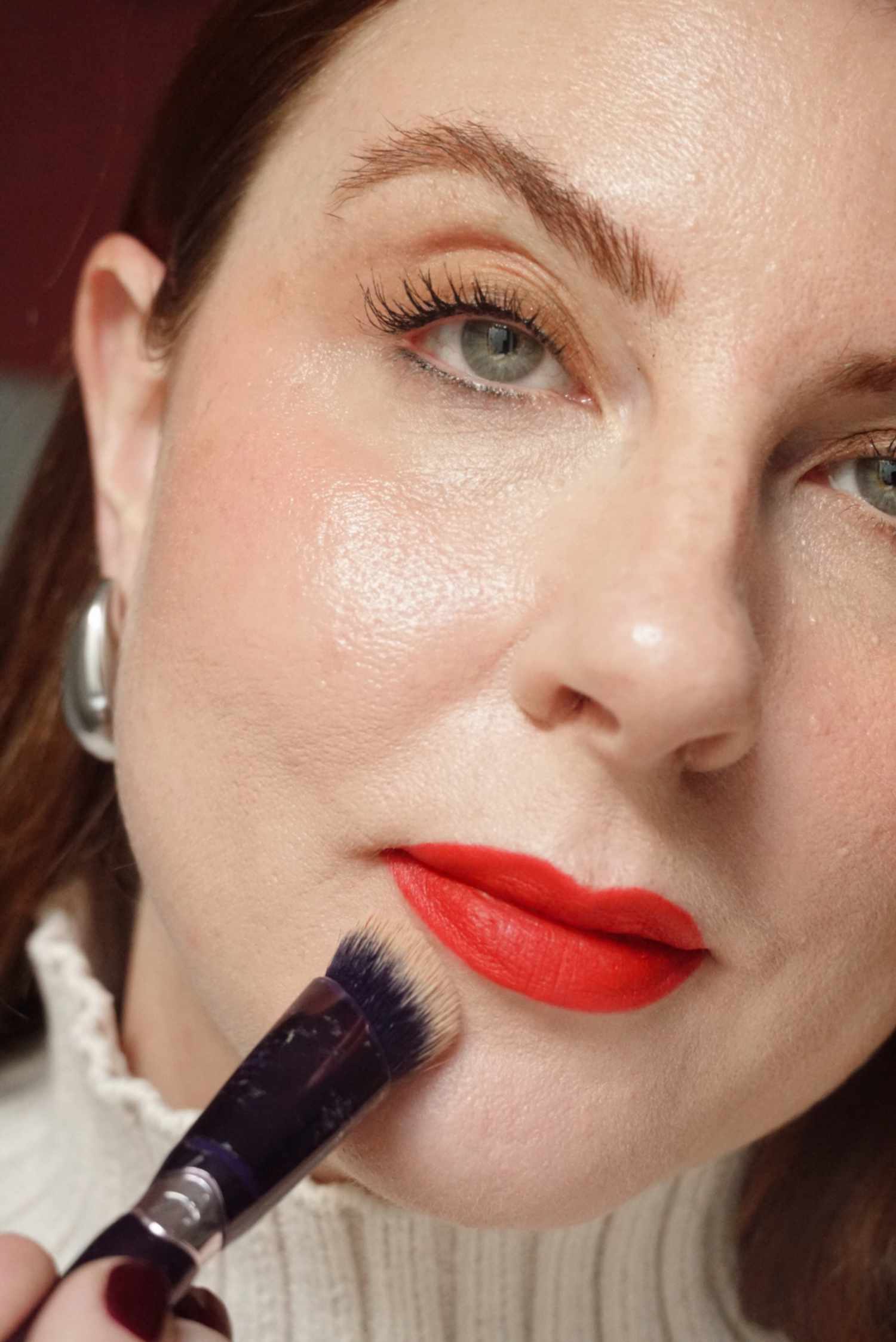 woman applying concealer with a brush around the edges of her red lips