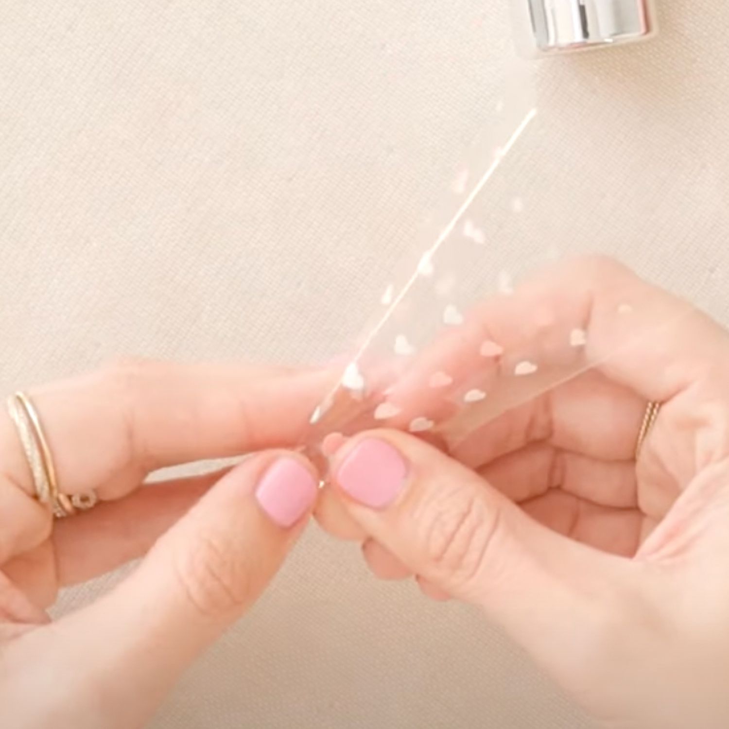 Person with pink manicure peeling heart nail stickers off a clear sheet