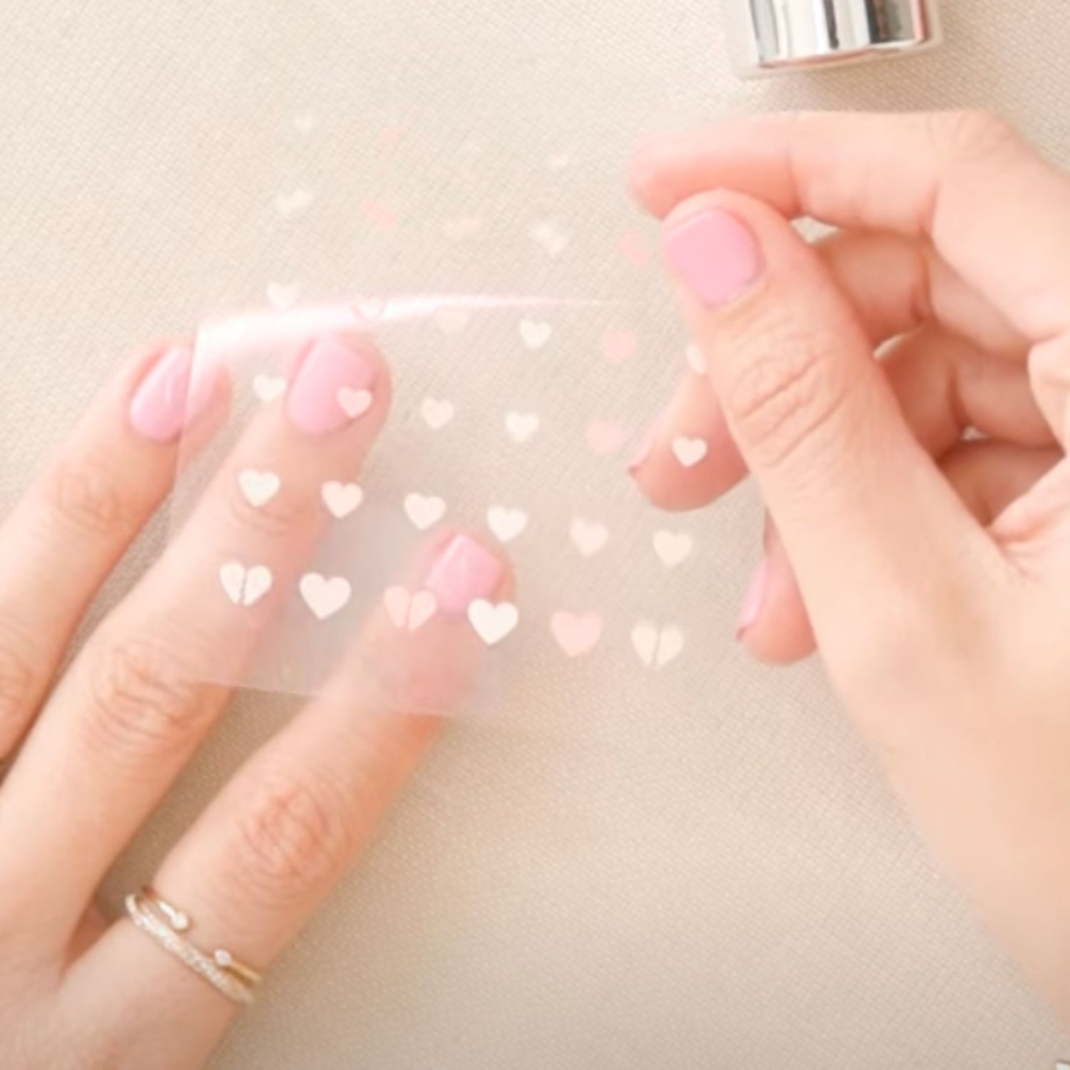 Close-up of hands with pink manicure holding clear sticker sheet with pale heart nail stickers