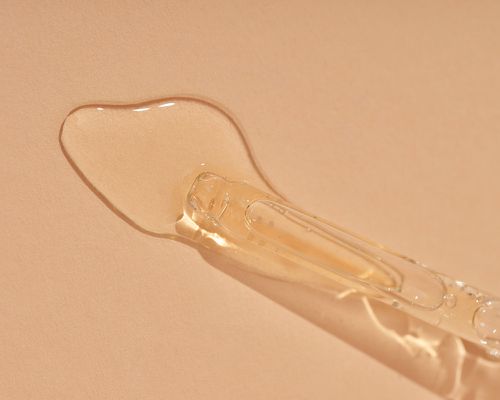 Close up of a dropper with pale yellow liquid on a blush background.