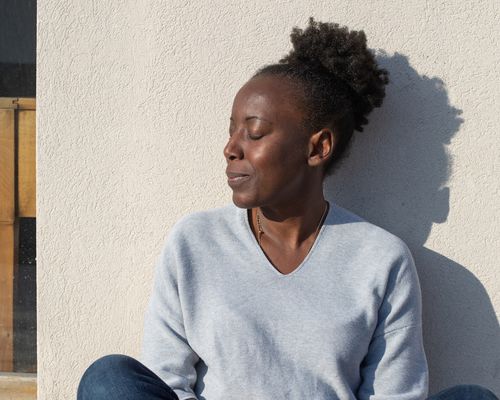 woman sitting against white wall in sunlight 