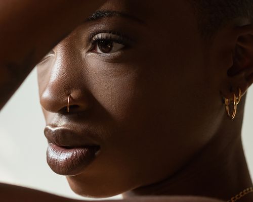 A young woman touches her head, piercings visible in her ears and nose