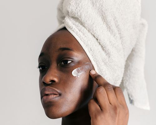 woman with towel on head applying face cream