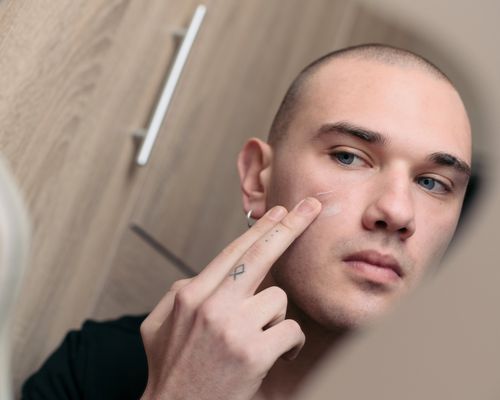 Man applying skincare products in mirror