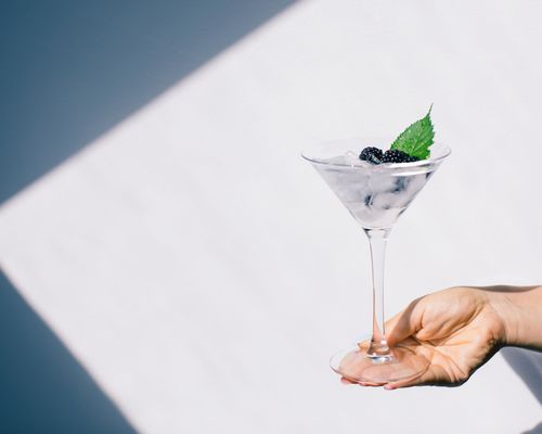 A clear alcoholic beverage in a martini glass, garnished with blueberries