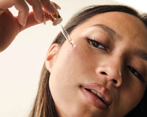 Woman applying a serum, head to the side looking downward.