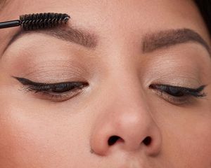 Close up of woman with winged liner and fluffy eyebrows being groomed with spoolie brush