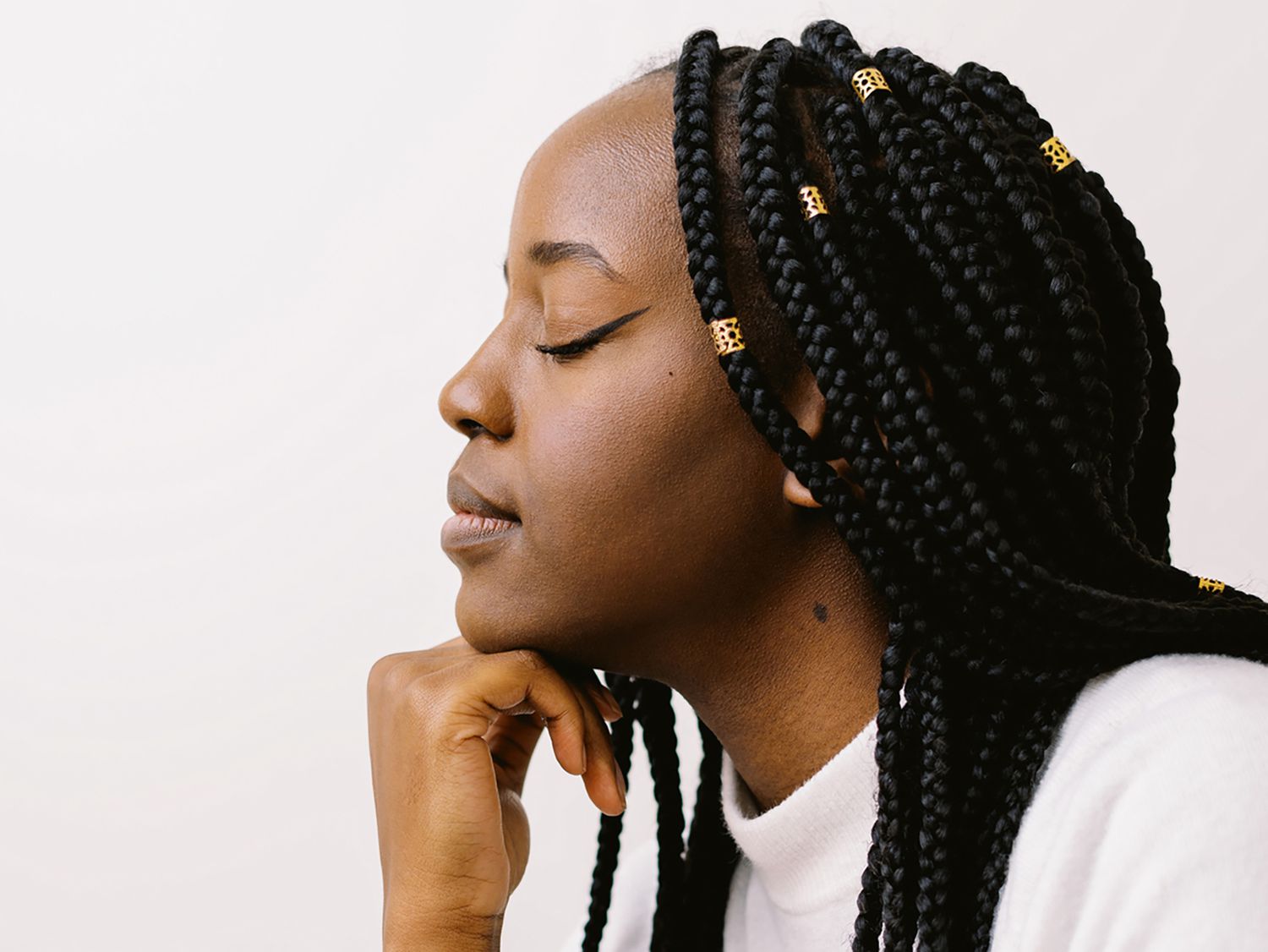 Side profile of a woman with long braids, hand on her chin, eyes closed