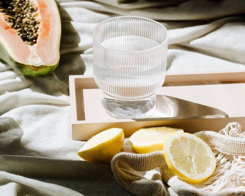 glass of water next to lemons and papaya 