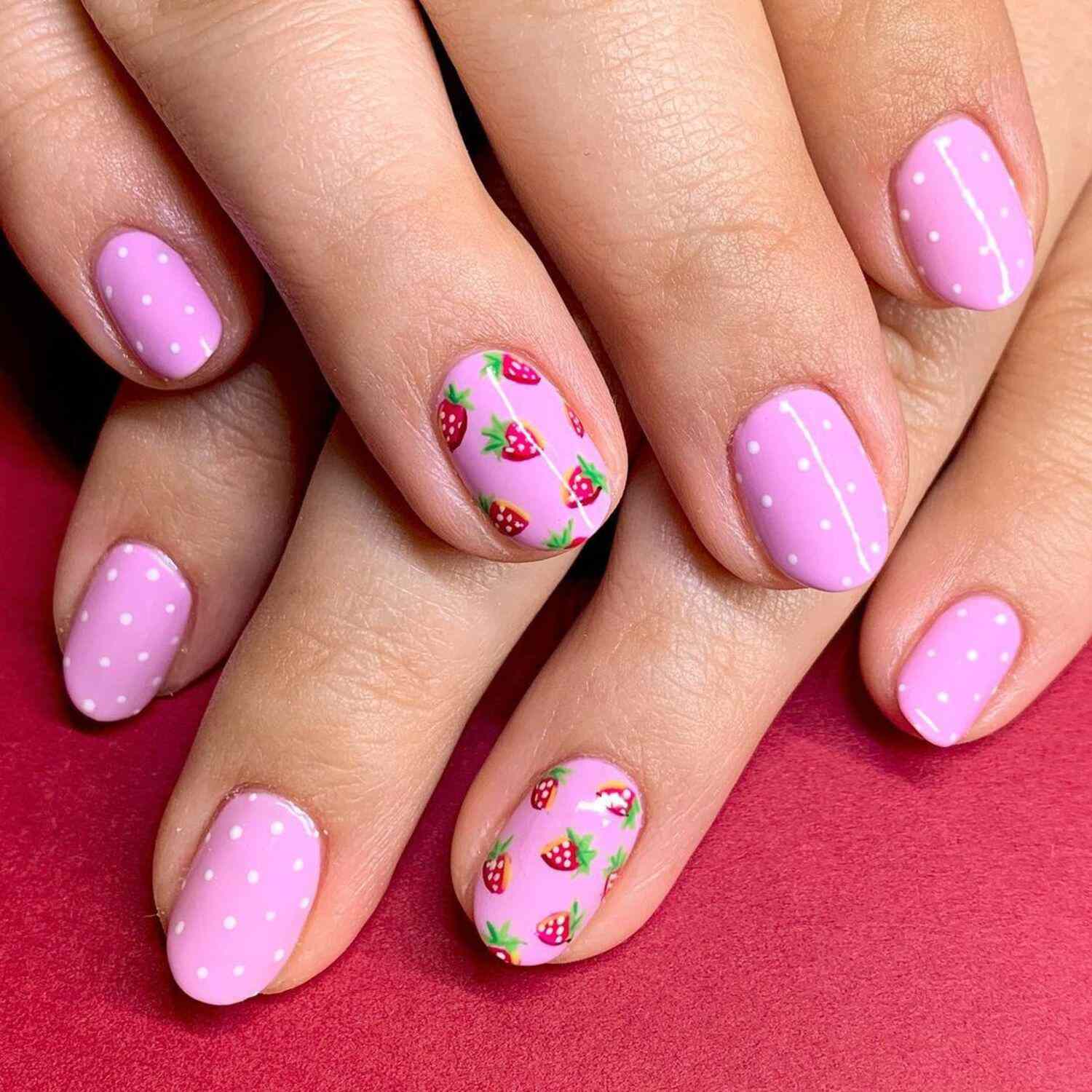 A baby pink manicure with strawberry and white polka dot details