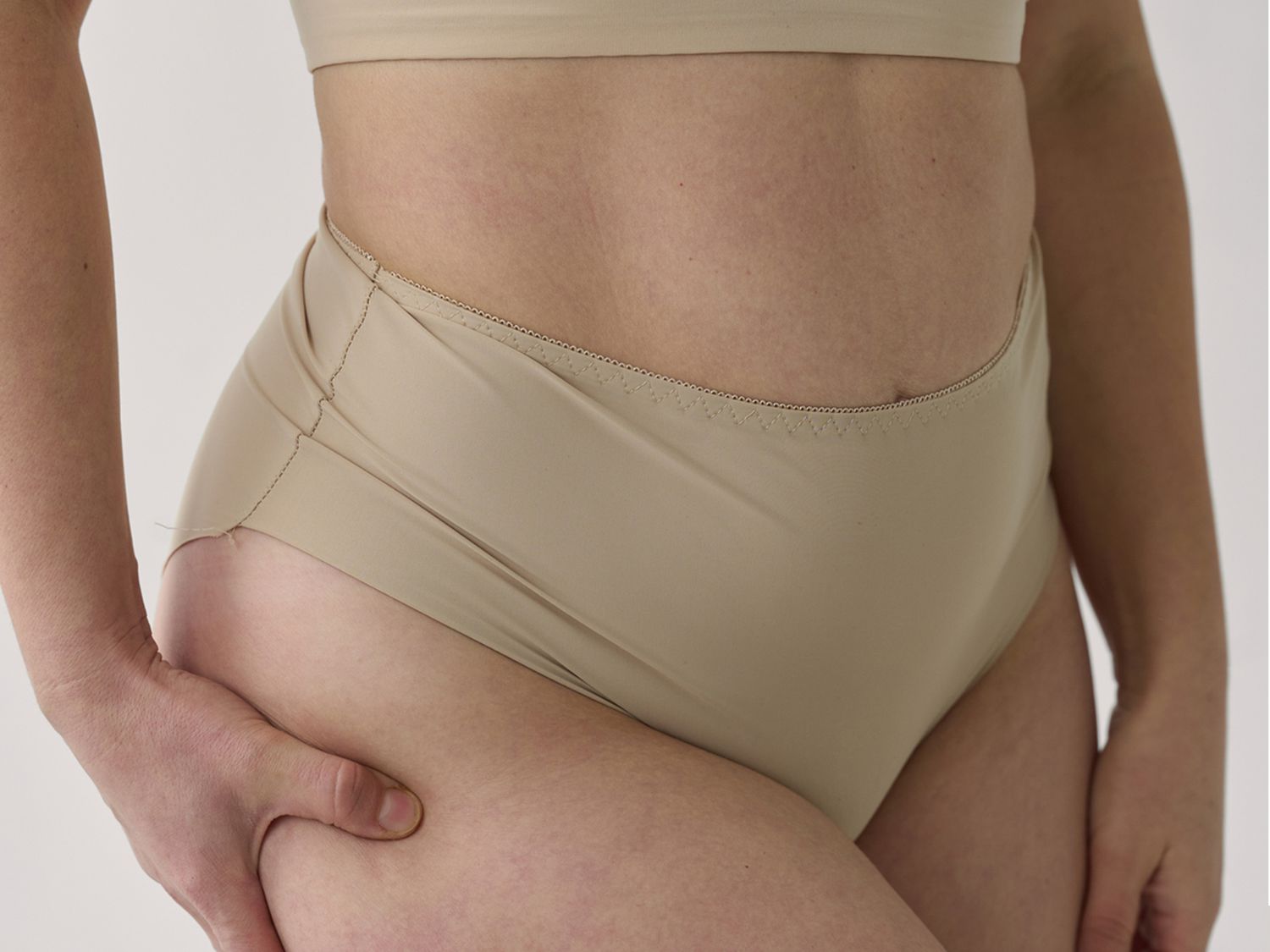 woman in neutral undergarments holding her thigh