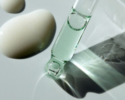 A liquid dropper up close, with drops of skincare in the background