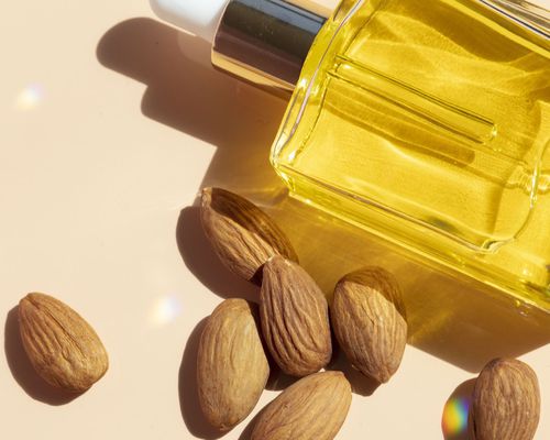 Bottle of skincare oil with pile of whole almonds