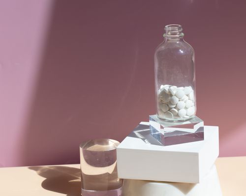 white pills in a glass bottle on top of marble blocks against a pink background