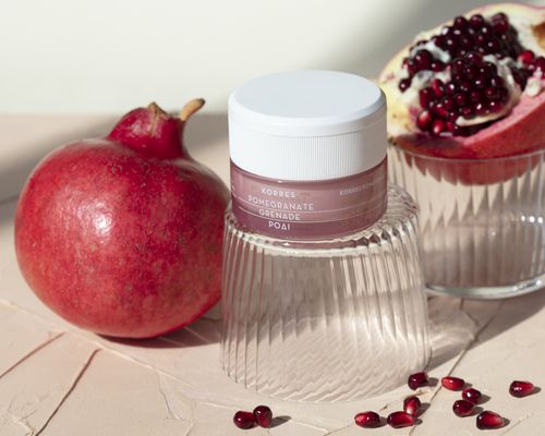 Pomegranates and pomegranate seeds flank a pink skincare product