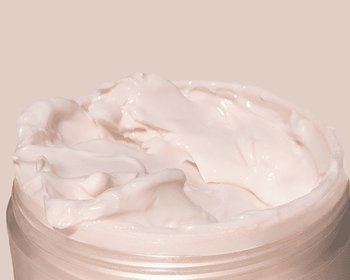 Light pink cream in a skincare container against a light pink background.