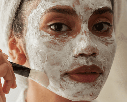 A woman applying a white mask paste to her face with a mask brush. 