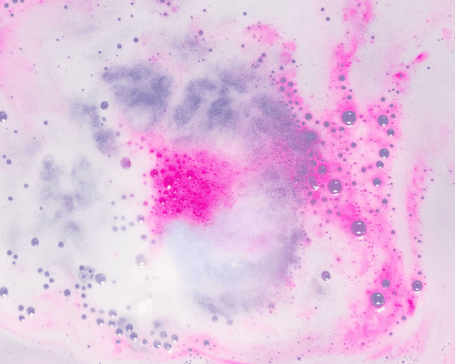 close up of pink bath bomb fizzing in tub water