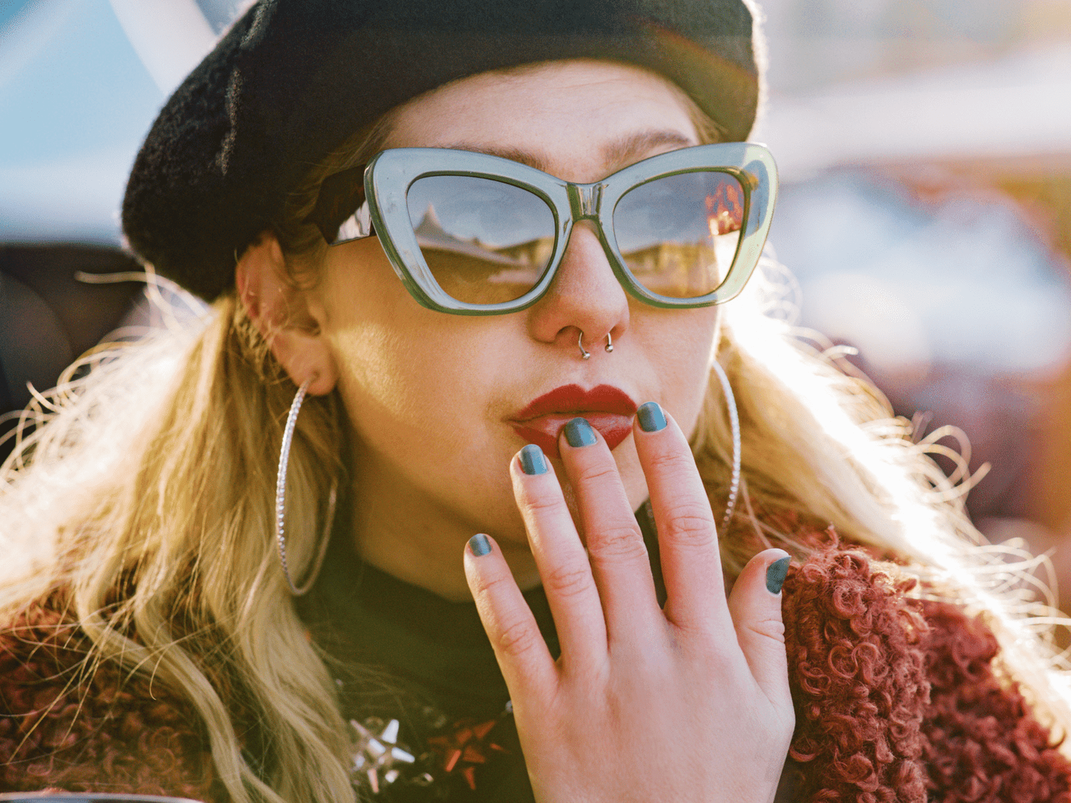 A woman wearing a beret, green sunglasses, red lipstick and hoop earrings