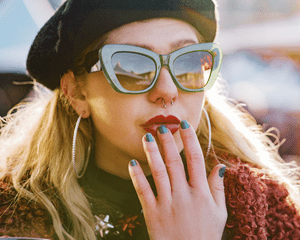 A woman wearing a beret, green sunglasses, red lipstick and hoop earrings