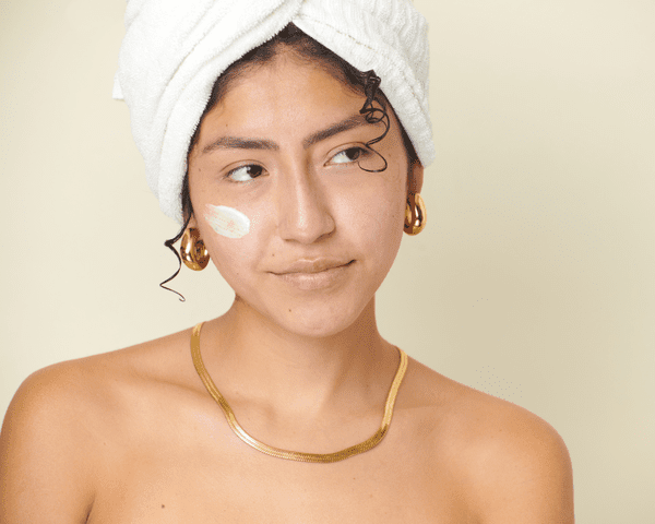 A woman with her hair wrapped in a towel and a swipe of cream on her face