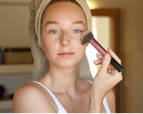 A woman applying blush with a makeup brush