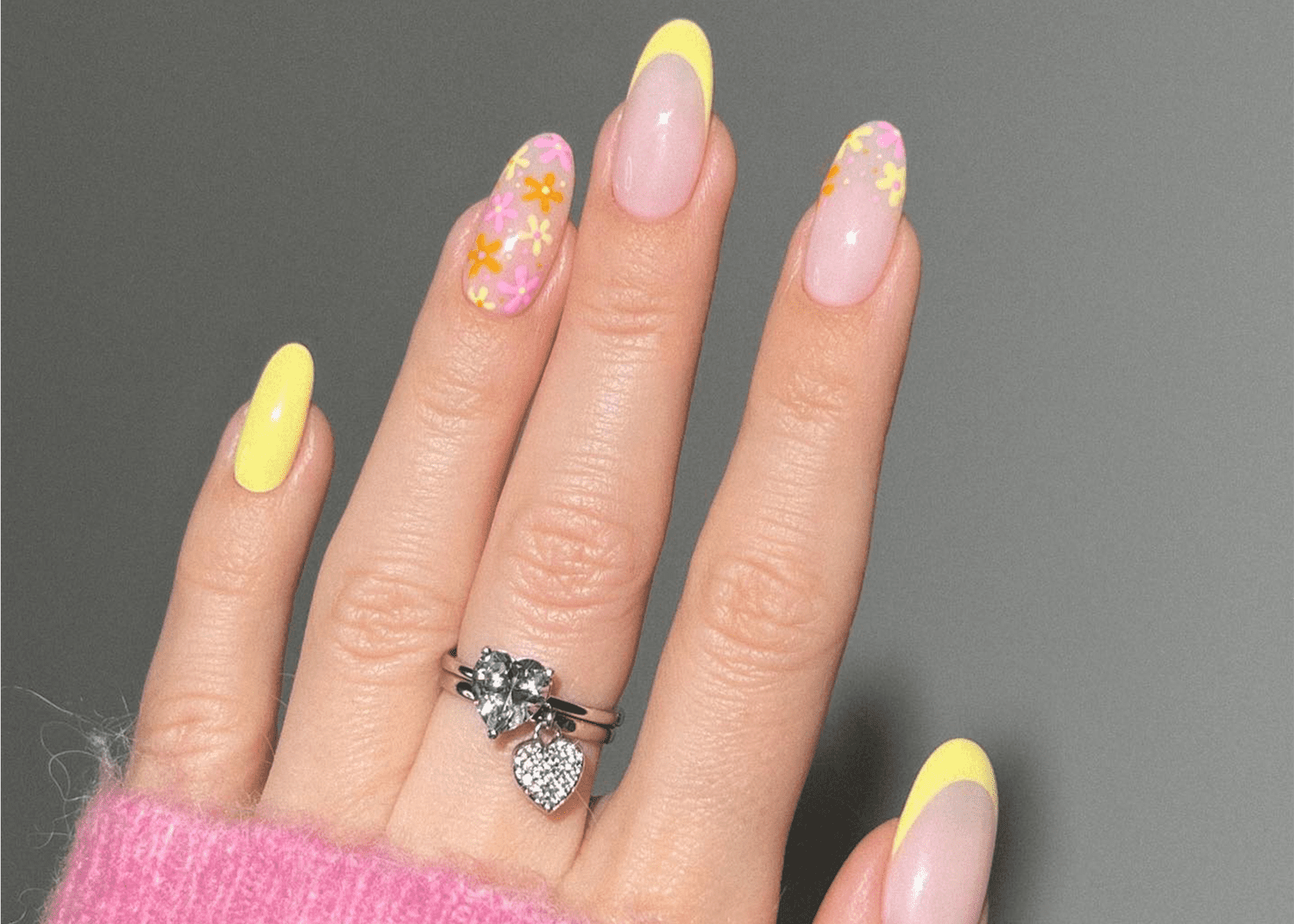 French nails with yellow tips. The ring finger and pointer finger do not have the French design and instead are covered in orange, pink, and yellow flowers. 