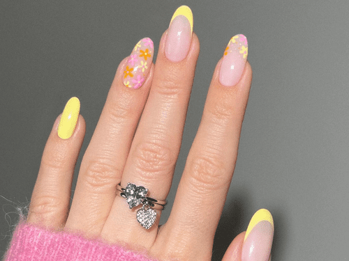 French nails with yellow tips. The ring finger and pointer finger do not have the French design and instead are covered in orange, pink, and yellow flowers. 