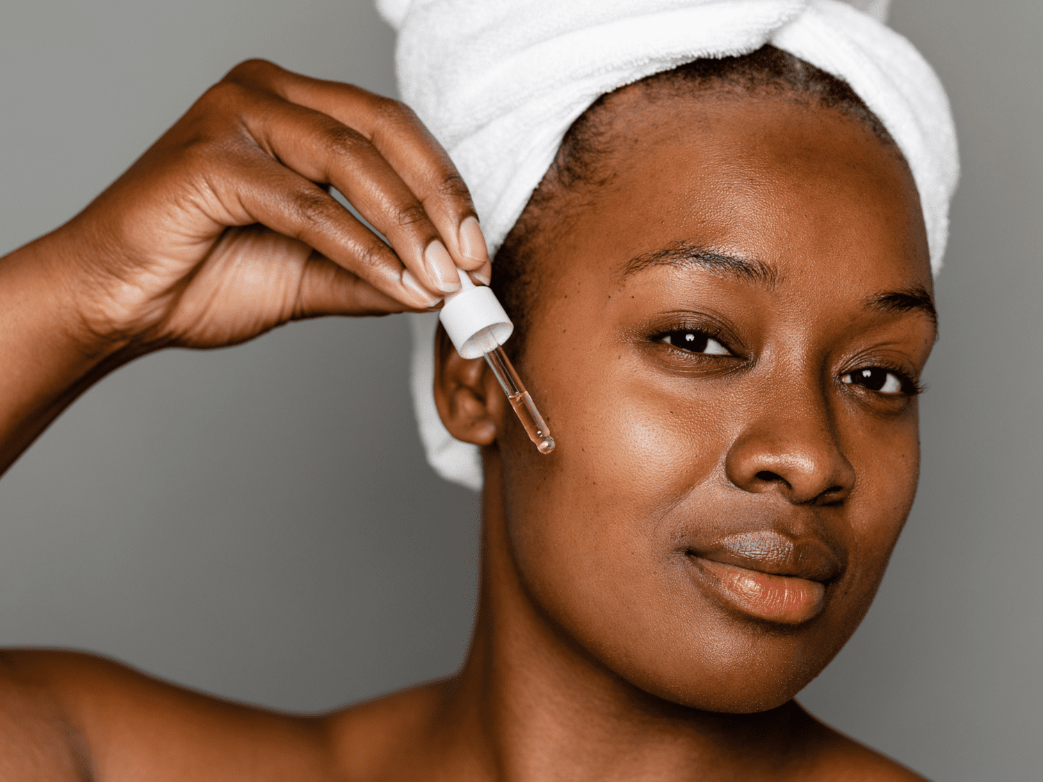 Close up of a woman holding a dropper of skincare to her face