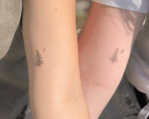 Friends with matching tattoos of a pine tree and crescent moon on upper arm