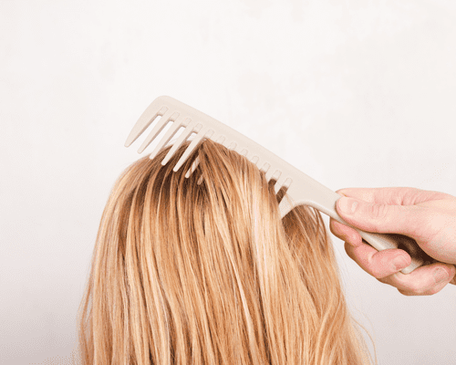 A hand holding a comb and brushing through blonde hair