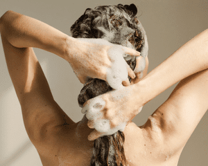 The back of a woman's head with suds in her hair and on her hands as she shampoos