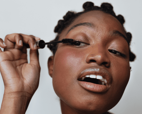 close up of woman applying mascara against grey background